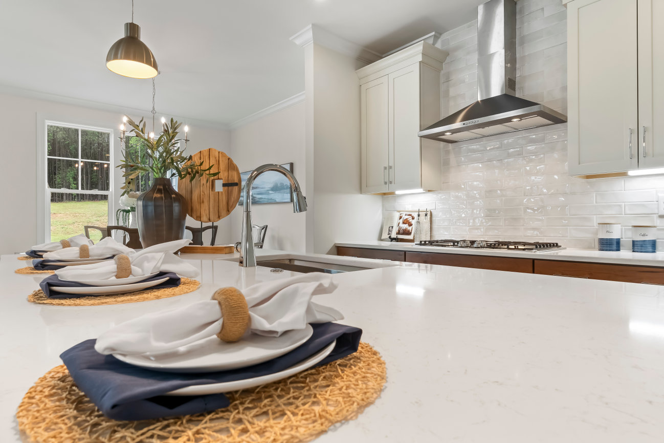 Modern kitchen with island, white cabinets, stainless range hood, and set dining place settings