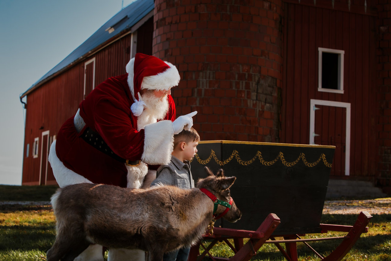 Santa points into the distance as a child and a reindeer stand beside his sleigh during an earlier holiday experience